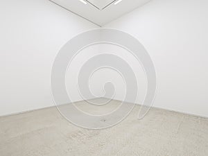 A view of a white painted interior of an empty room or an art gallery with a fluorescent lighting and concrete floors