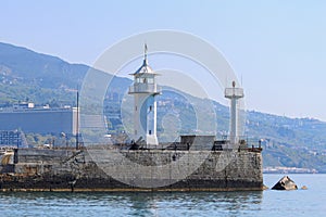 View of the white tower of the old lighthouse in Yalta. In the background of the visitors, the mountains and the sky.