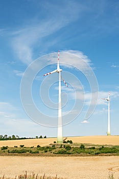 View of a wind power plant on a background of blue sky and fields with grain crops. The concept of environmental electricity produ