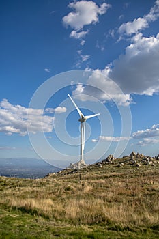 View of a wind turbine on top of mountains, blue sky as background