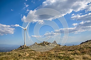 View of a wind turbine on top of mountains, blue sky as background