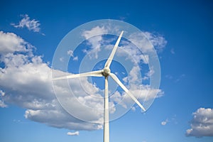 View of a wind turbine on top of mountains, blue sky as background