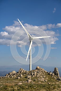 View of a wind turbine on top of mountains, blue sky as background