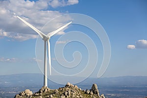 View of a wind turbine on top of mountains, blue sky as background