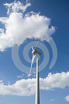 View of a wind turbine on top of mountains, blue sky as background