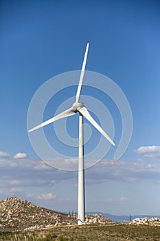 View of a wind turbine on top of mountains, blue sky as background