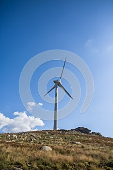 View of a wind turbine on top of mountains, blue sky as background