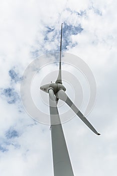 View of a wind turbine on top of mountains, cloudy sky as background