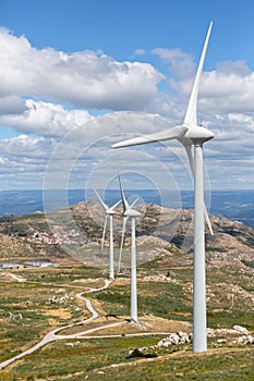 View of a wind turbines on top of mountains, dirt road and wild nature and landscape, cloudy sky as background