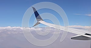 A view through a window of an airplane wing as it flies above a fluffy cloudy sky