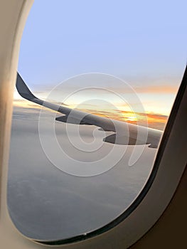 View from window on airplane wing plane while flying above dawn clouds, sun rises on horizon, plane flies over sea, ocean,