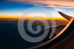 View through the window of the airplane on the wing and turbine at sunrise against the cloudy sky