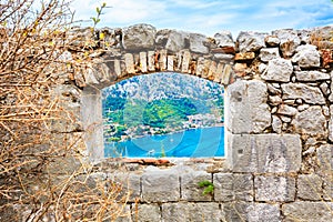 View through a window in ancient stone wall of a medieval fortress to the sea landscape and coast town.