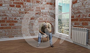 The view from the window of an empty room. The man is sitting on a stool