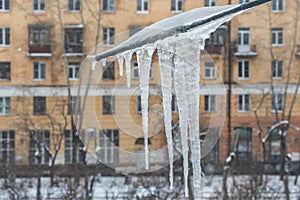 View through a window with a group of sharp bright white transparent icicles outside on TV antena to a street in winter