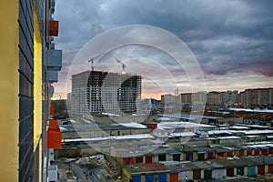 View from the window of a new house on the area under construction. Old and new city against the cloudy sky. Sunset in the