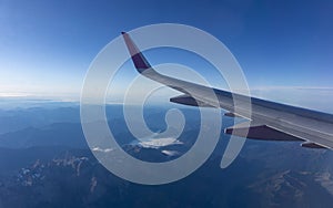 The view from the window of a passenger airliner flying over the territory of the Alps mountain range. Airplane wing on a