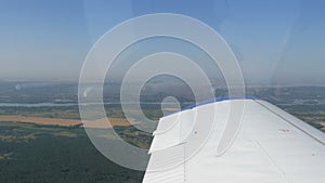 View from the window of a small passenger private plane against the backdrop of a white wing. Top view green fields and