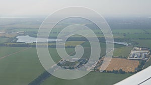 View from the window of a small passenger private plane against the backdrop of a white wing. Top view green fields and