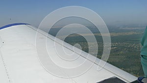 View from the window of a small passenger private plane against the backdrop of a white wing. Top view of houses, green