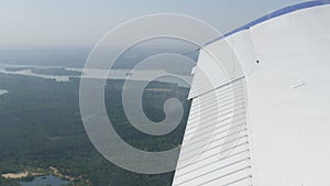 View from the window of a small passenger private plane against the backdrop of a white wing. Top view of houses, green