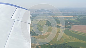 View from the window of a small passenger private plane against the backdrop of a white wing. Top view yellow fields