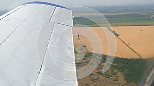 View from the window of a small passenger private plane against the backdrop of a white wing. Top view yellow fields