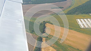 View from the window of a small passenger private plane against the backdrop of a white wing. Top view yellow fields