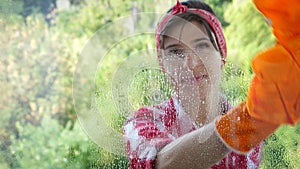 View through the window, smiling Beautiful woman in gloves, Cleaning Window by spraying Cleaning Products, using