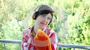 View through the window, smiling woman in headphones, in gloves, Cleaning Window by spraying Cleaning Products, using