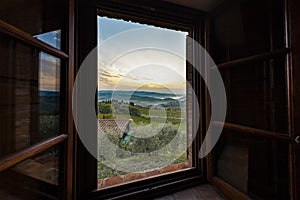 View through a window to a sunrise over foggy hills in Tuscany