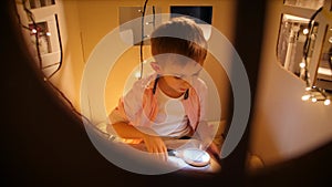 View through window of toy house on little boy reading book at night. Concept of child education and reading in dark