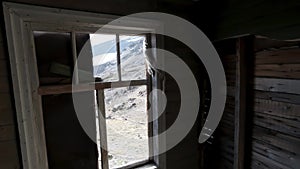 View through the windows inside a wooden abandoned house. Clip. Old ruined wooden building and a hill slope outside.