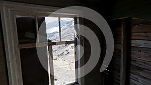 View through the windows inside a wooden abandoned house. Clip. Old ruined wooden building and a hill slope outside.