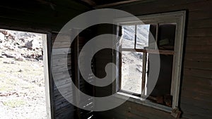 View through the windows inside a wooden abandoned house. Clip. Old ruined wooden building and a hill slope outside.