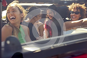 View Through Windscreen Of Group Of Laughing Female Friends Having Fun In Open Top Car On Road Trip