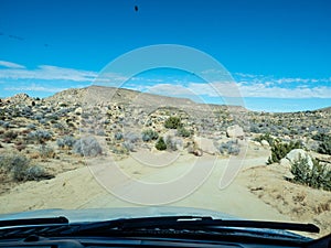 View through windshield on dirt desert road with yuccas blue sky sun in Yucca Valley California near Joshua Tree National Park