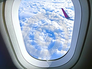 View of wing of an airplane flying above the clouds. Clouds and sky through an airplane window