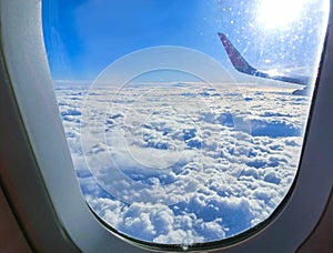 View of wing of an airplane flying above the clouds. Clouds and sky through an airplane window