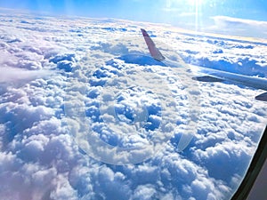 View of wing of an airplane flying above the clouds. Clouds and sky through an airplane window