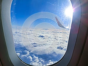 View of wing of an airplane flying above the clouds. Clouds and sky through an airplane window