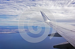 View of the wing of an airplane flying above the clouds at high altitude under a blue sky from the passenger window. In flight photo