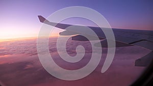 View Of Wing Of Airplane Flying Altitude Over Clouds With Scarlet Sunset Sky