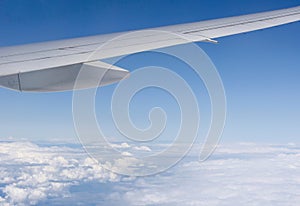 View of wing of airplane with open flaps from window with blue sky above clouds background