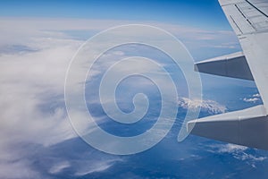 View of the wing of an airplane over the land with mountains and clouds