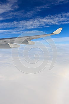 A view of wing of airplane from window above clouds and blue sky