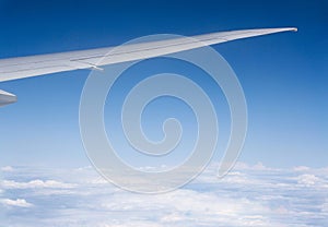 View of wing of airplane from window with blue sky above clouds background