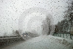 View on winter road and car through wet windshield with rain drops