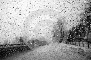 View on winter road and car through wet windshield with rain drops. Black and white