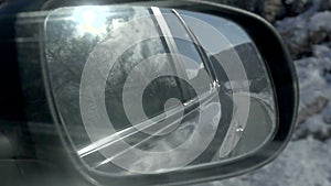 View of the winter road in the rearview mirror of a car. Sun in the clouds